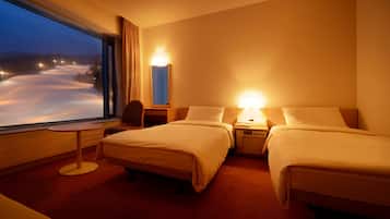 A hotel room with two beds, a small table, a chair, a nightstand with a lamp, and a window with a view of a snowy landscape.