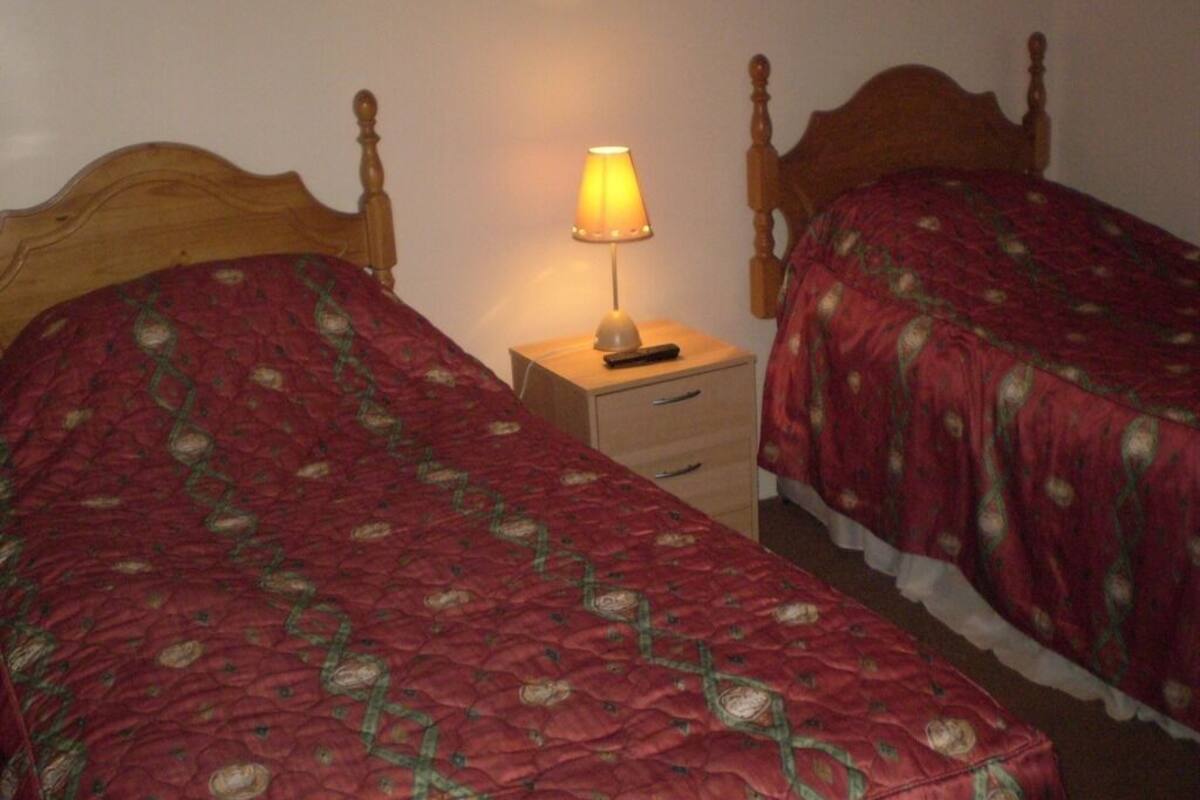 A bedroom with two wooden beds, a nightstand with a lamp, and a drawer unit.