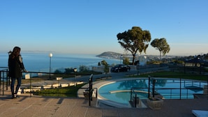 A pool area with a view of the sea, a person standing by the pool, and a car parked nearby. - Golden Carthage Residence (La Marsa)