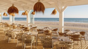 Een terras met tafels en stoelen, met uitzicht op een strand.
