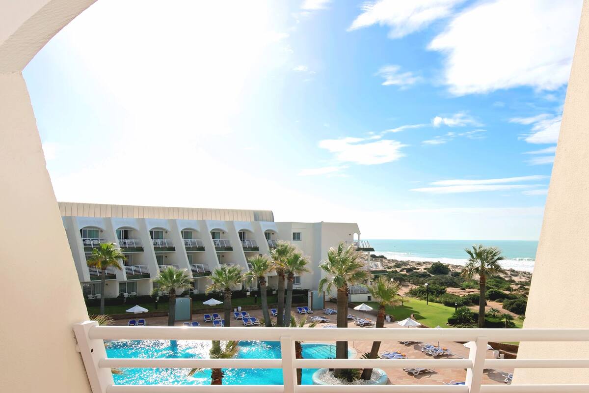 Een hotel met een zwembad, ligbedden en uitzicht op het strand.