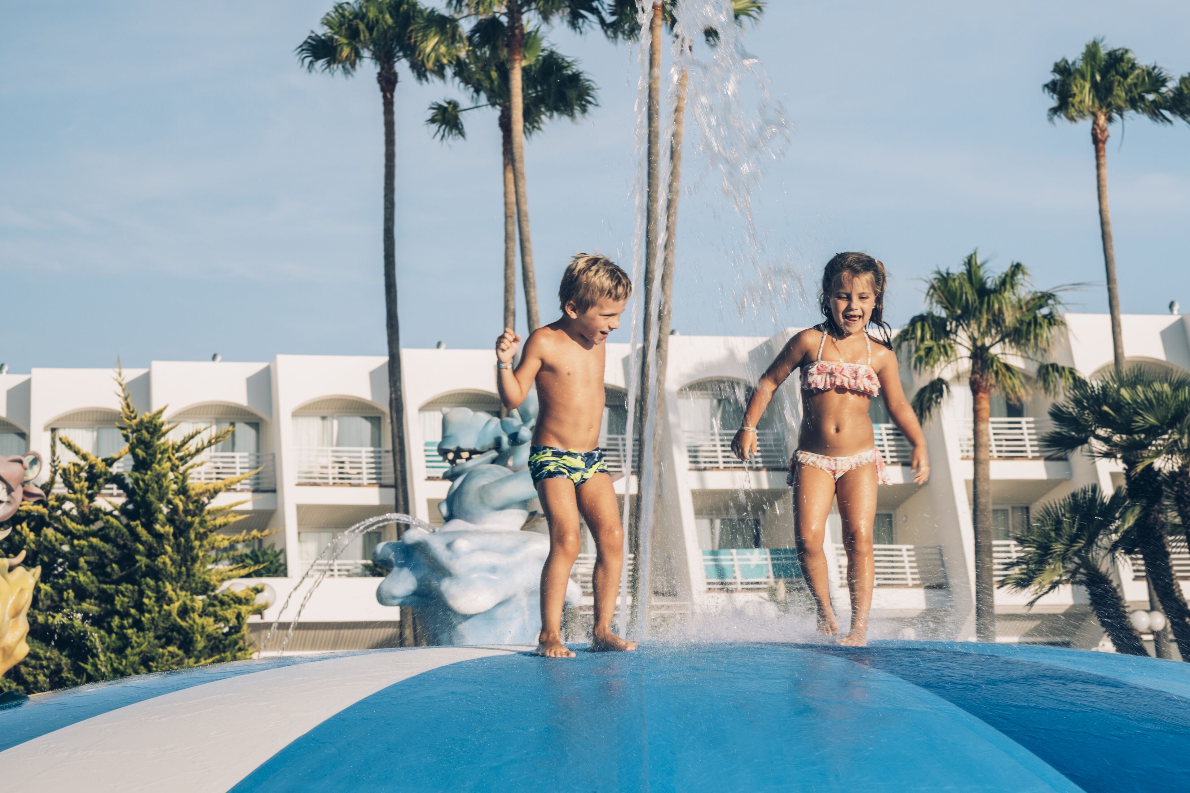 Une zone avec une piscine, des palmiers et un bâtiment doté de balcons en arrière-plan.