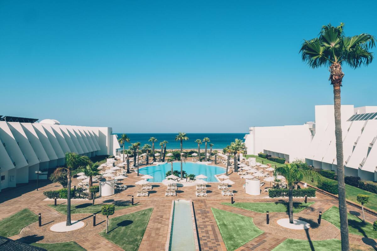 Een resort met een centraal gelegen zwembad, palmbomen en uitzicht op de oceaan.