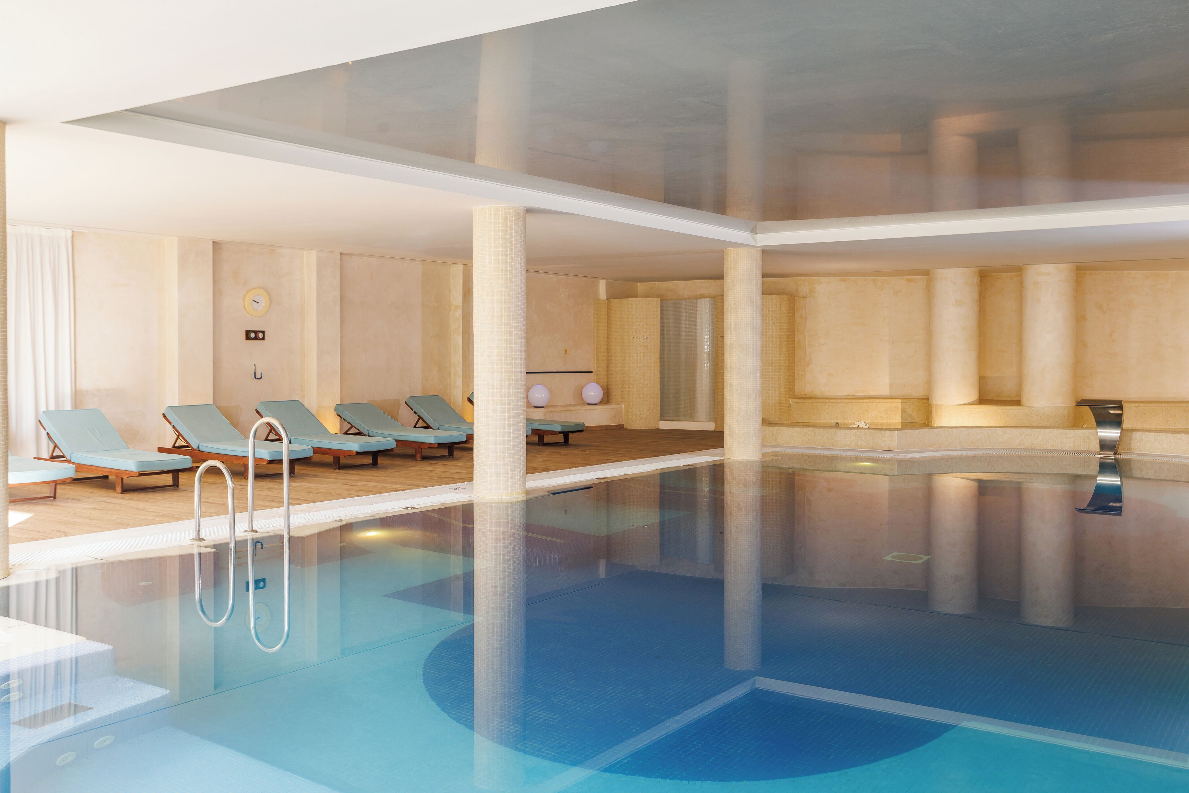Une piscine intérieure moderne avec de l’eau cristalline, des chaises longues et un cadran solaire mural.