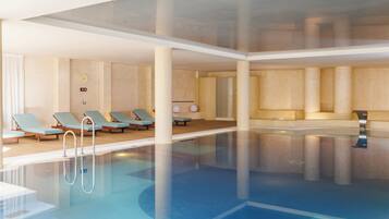 A modern indoor swimming pool with clear water, lounge chairs, and a sun clock on the wall.