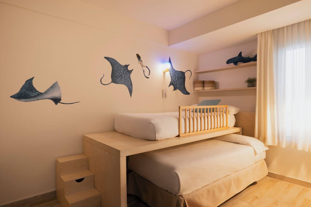 Een kinderkamer met een stapelbed, een wandplank en decoratieve wandkunst.