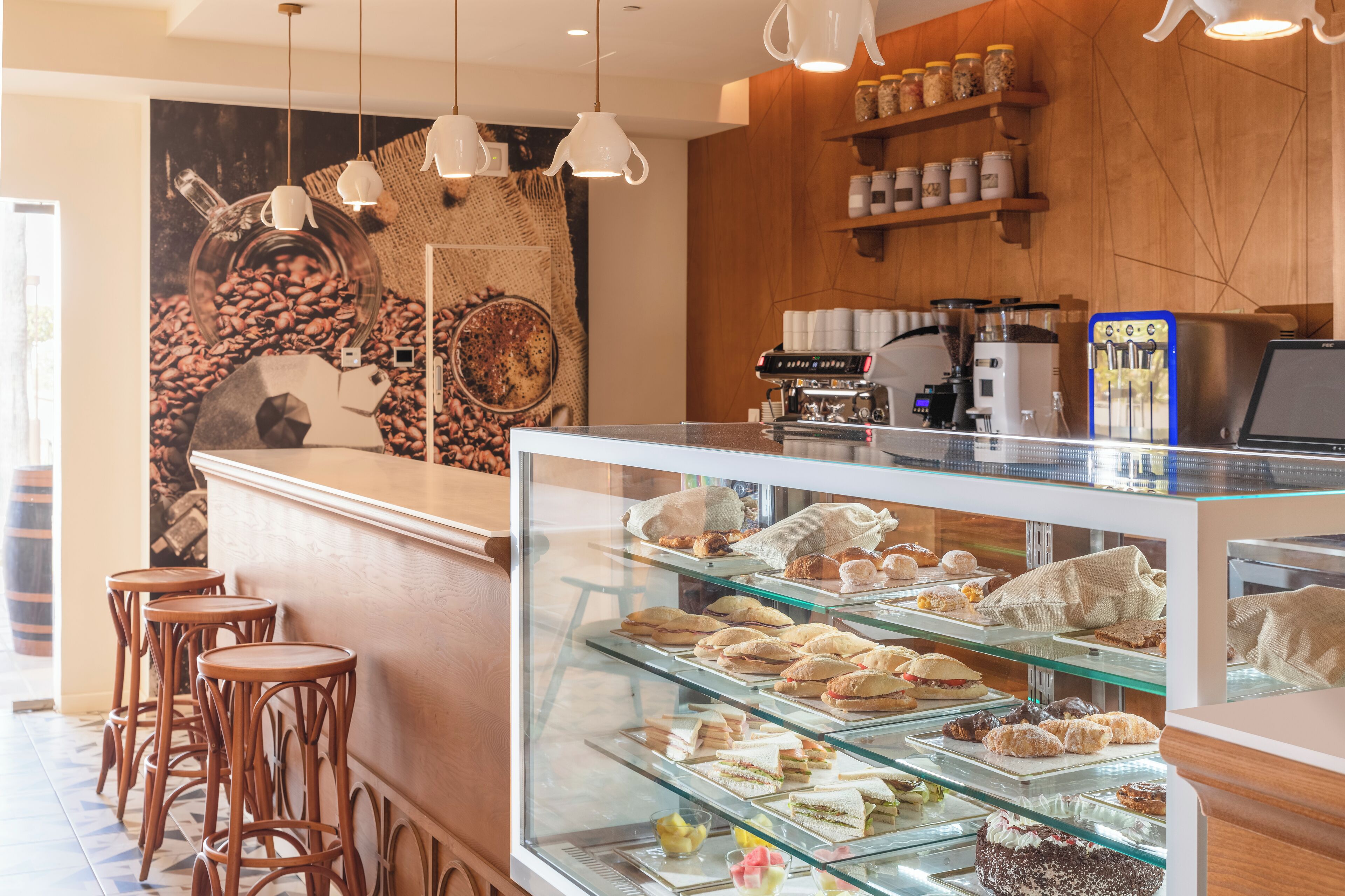A café with a coffee machine, a display case with pastries, and wooden bar stools.