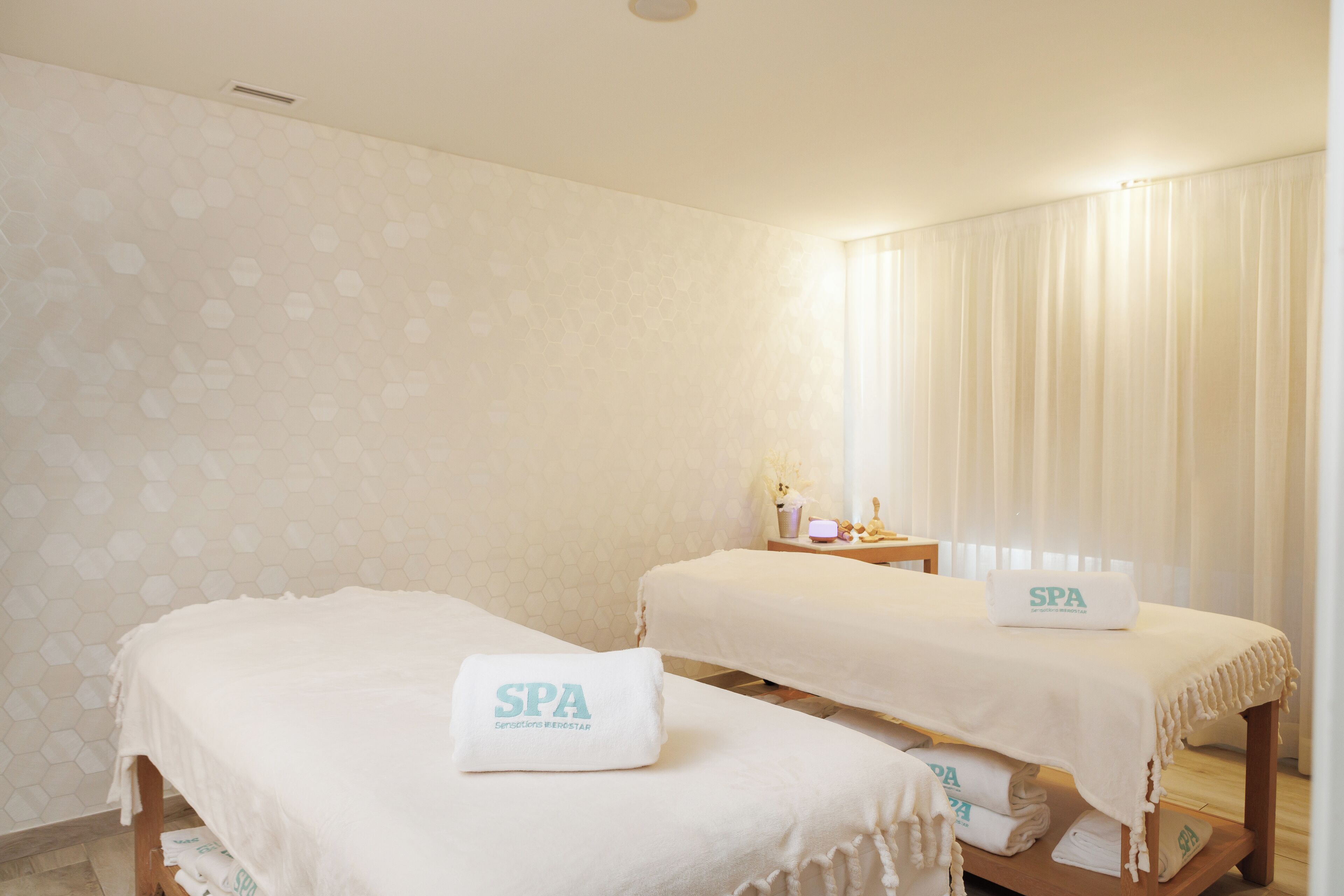 Une salle de spa équipée de deux lits, chacun agrémenté d’une serviette étiquetée « SPA » et d’une petite table sur laquelle se trouvent une lampe et des objets décoratifs.