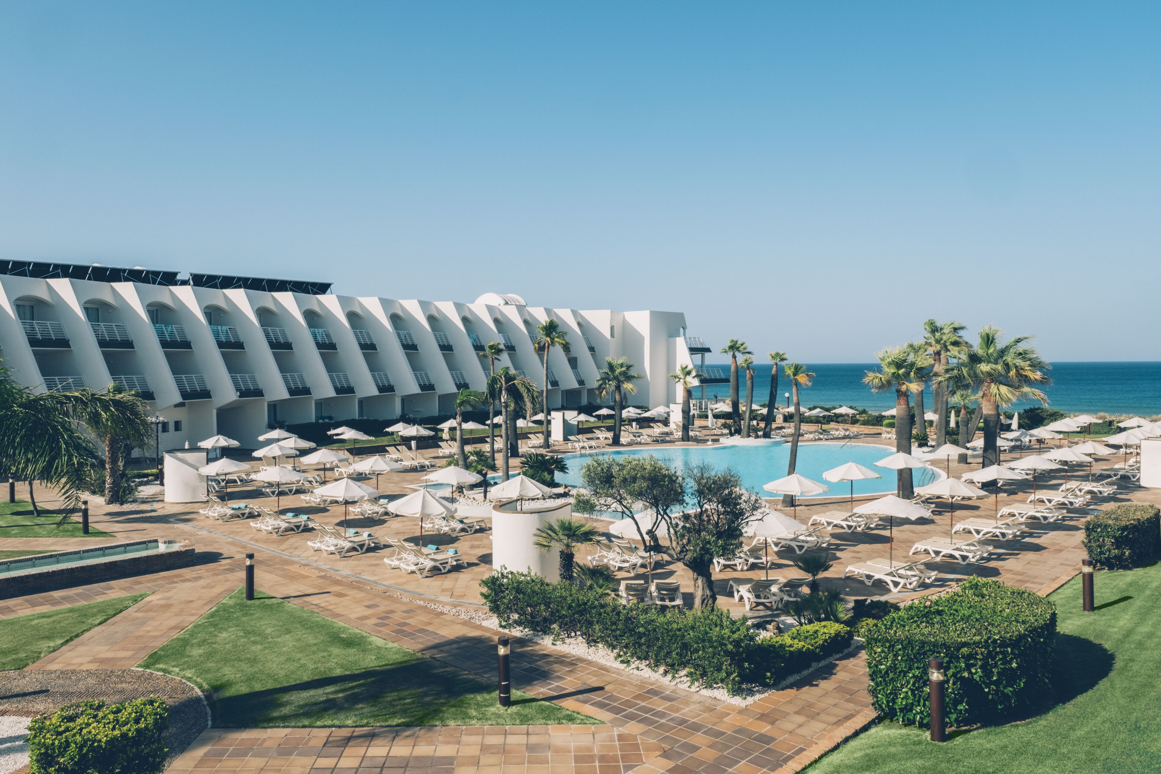 Een resort met een zwembad, ligbedden, parasols en palmbomen.