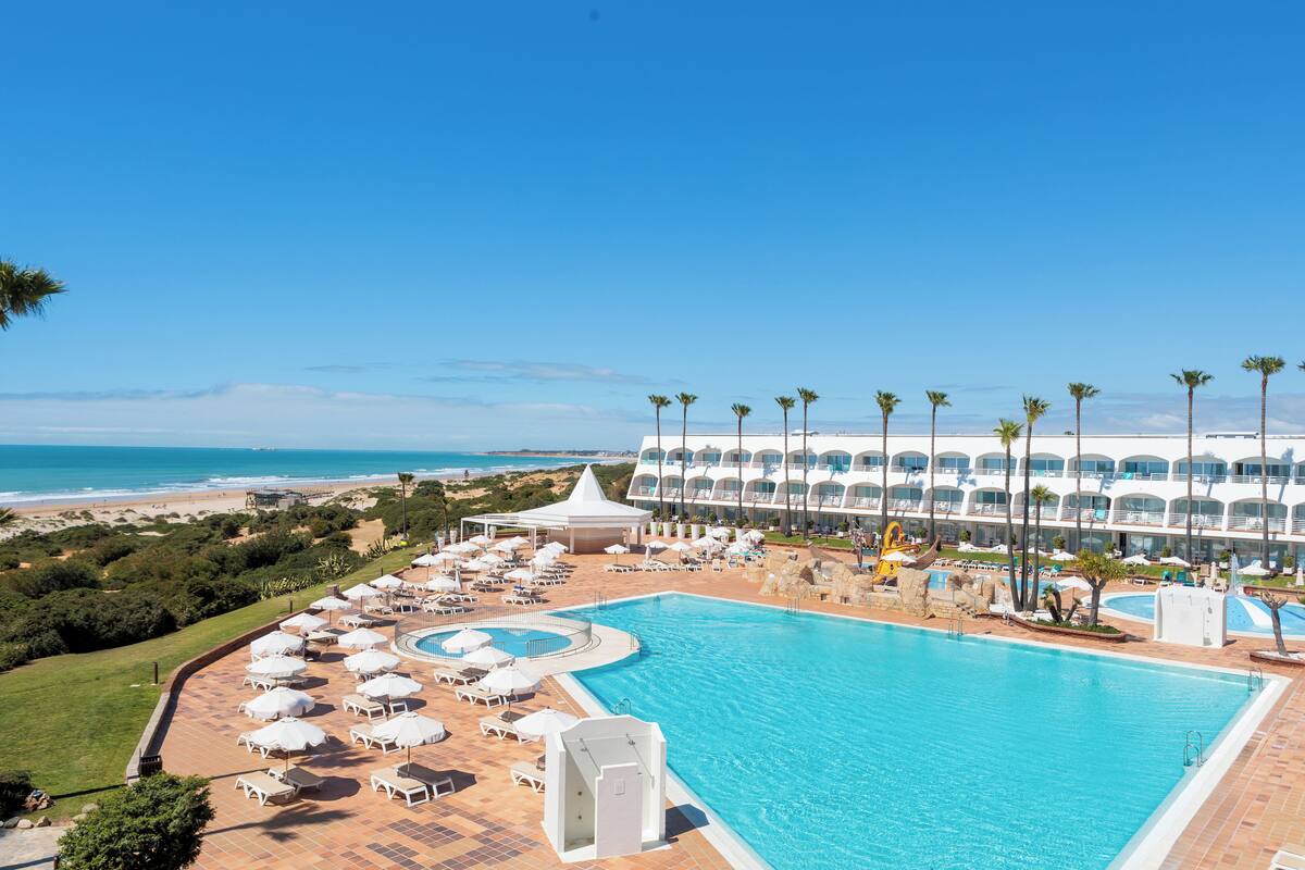 Een resort met een groot zwembad, ligbedden en uitzicht op het strand.