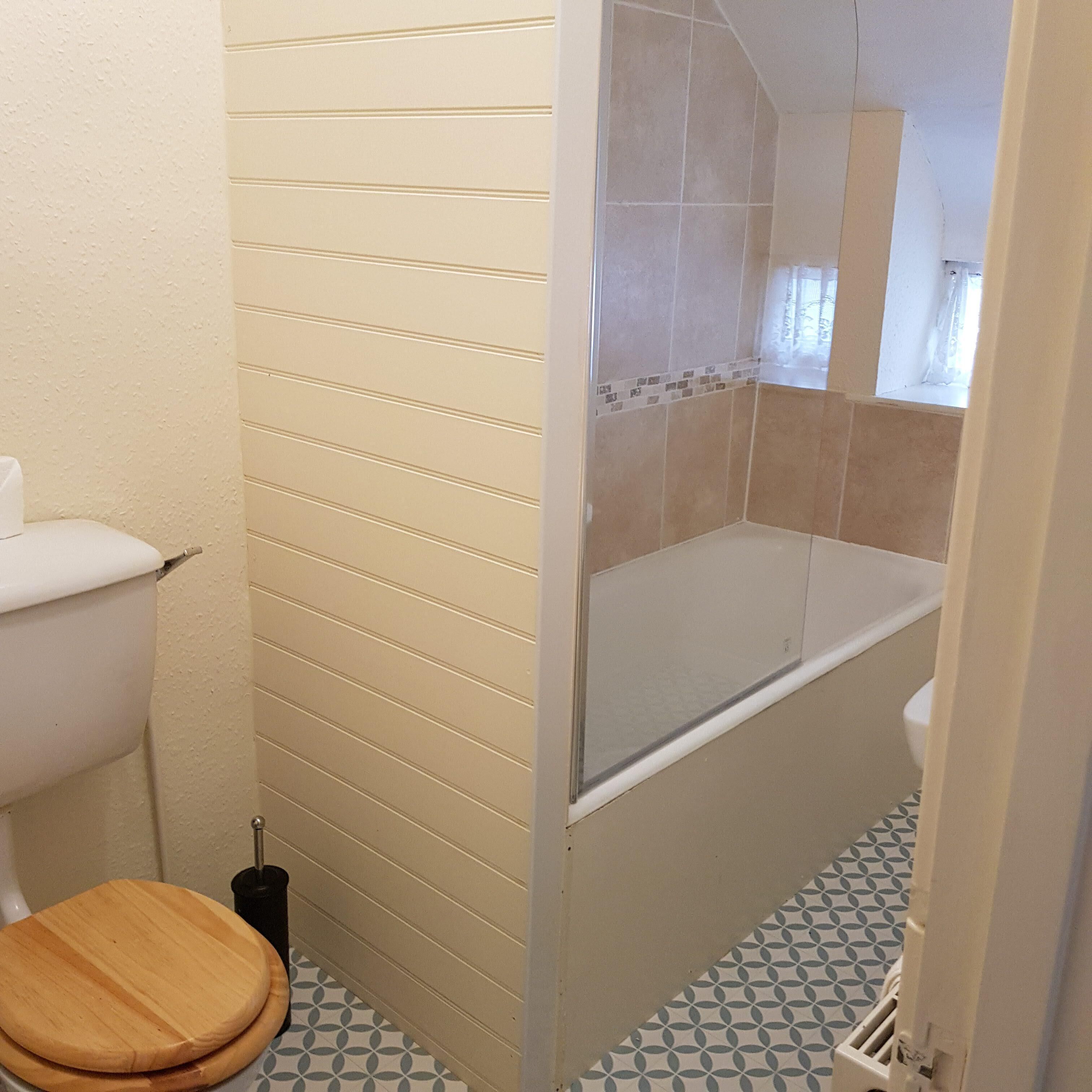 Un baño con inodoro, asiento de madera, ducha con puerta de cristal y baldosas de suelo con diseño.