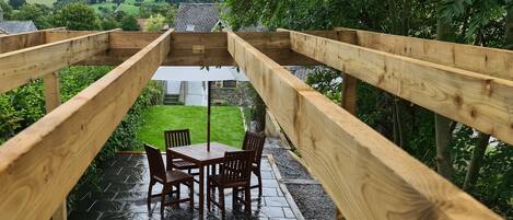 A wooden deck with a table and chairs, overlooking a green landscape with hills.