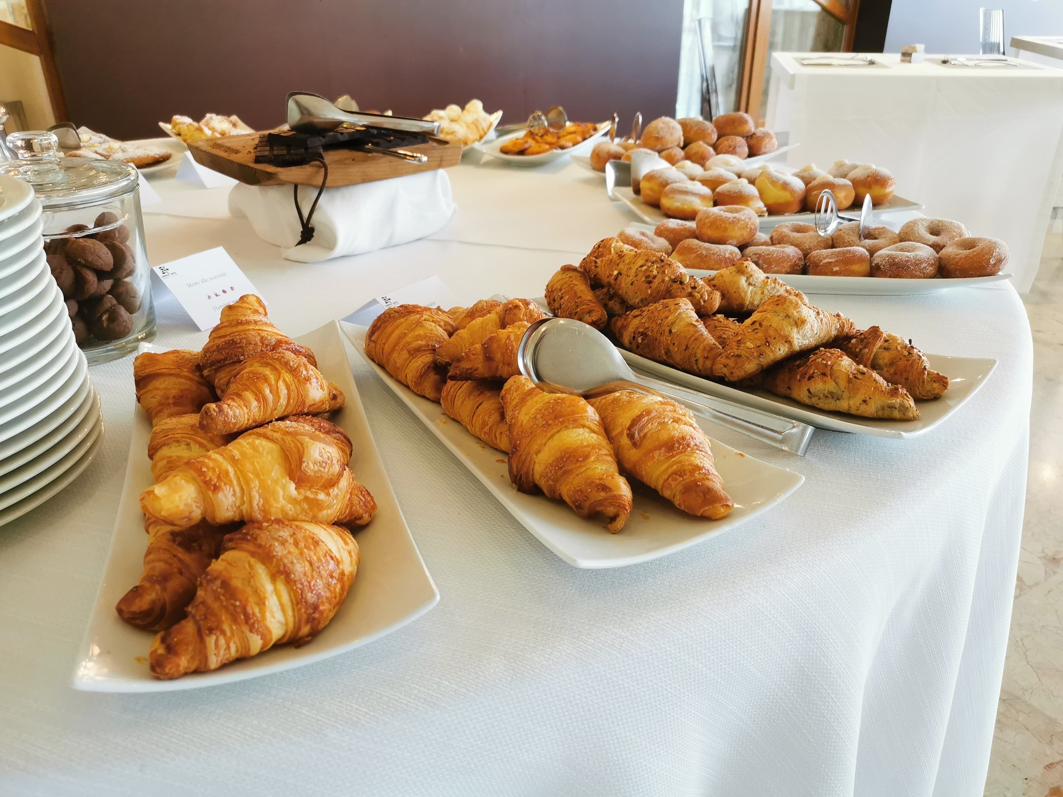 Una mesa de buffet con diversos pasteles, entre ellos cruasanes y rosquillas, y un tarro de chispas de chocolate.