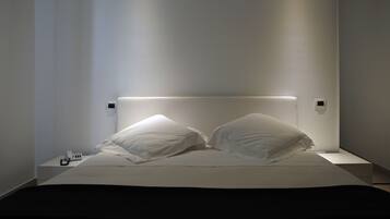 Een moderne slaapkamer met een bed, witte kussens en een nachtkastje met een lamp.