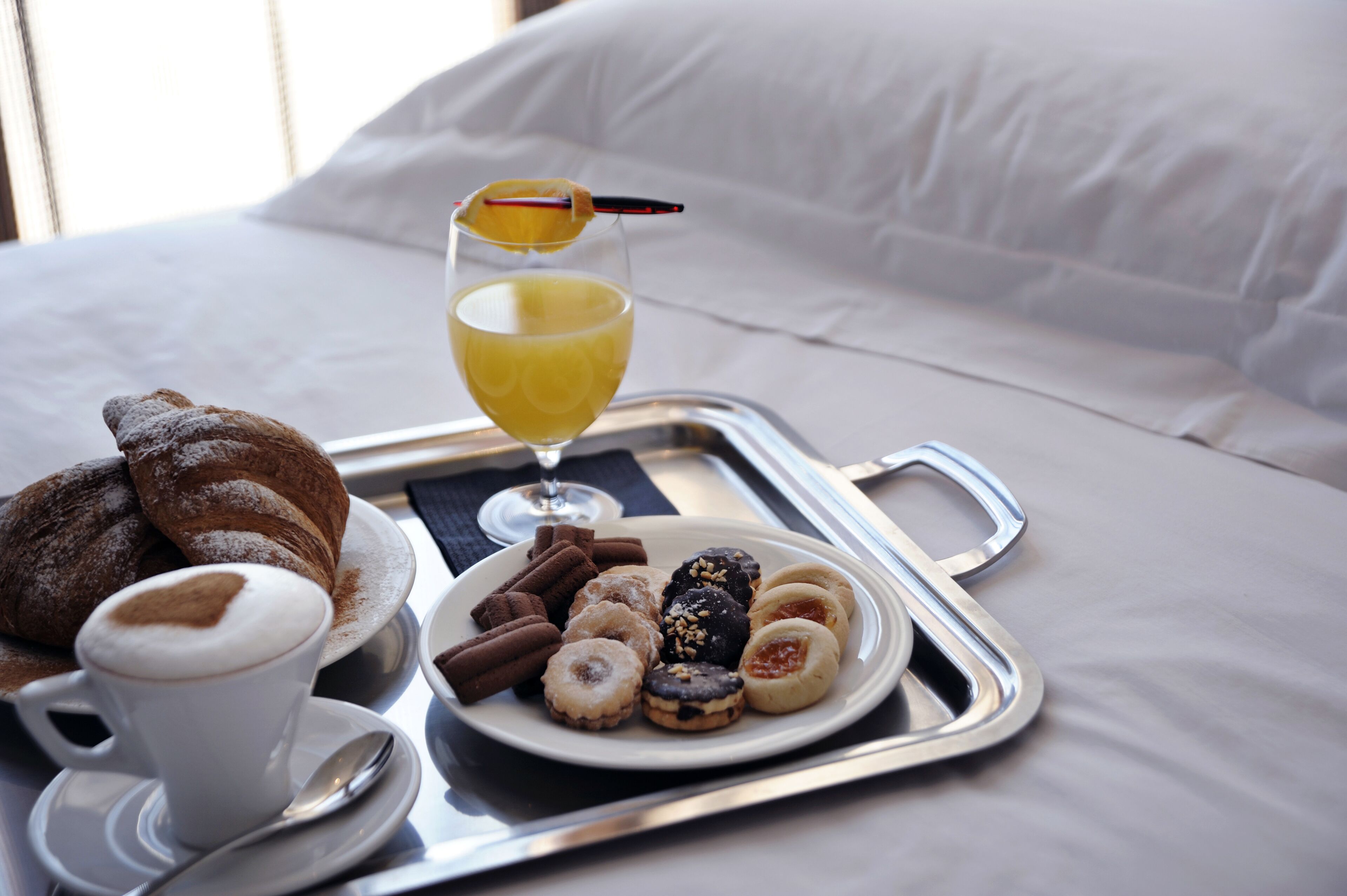 A tray with croissants, pastries, and a glass of orange juice on a bed.