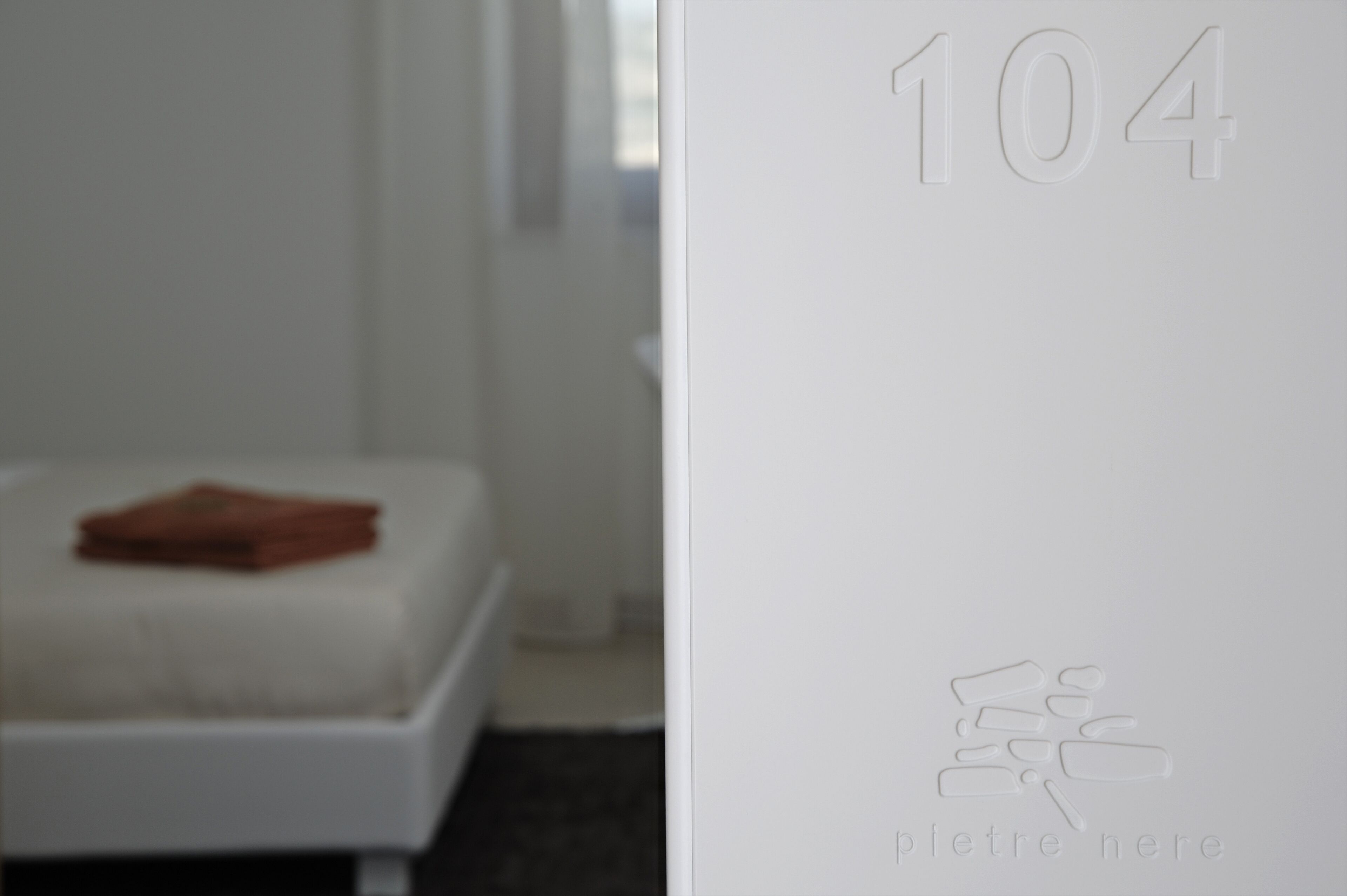 A white room with a bed and a wall with the number 104 and a small logo.
