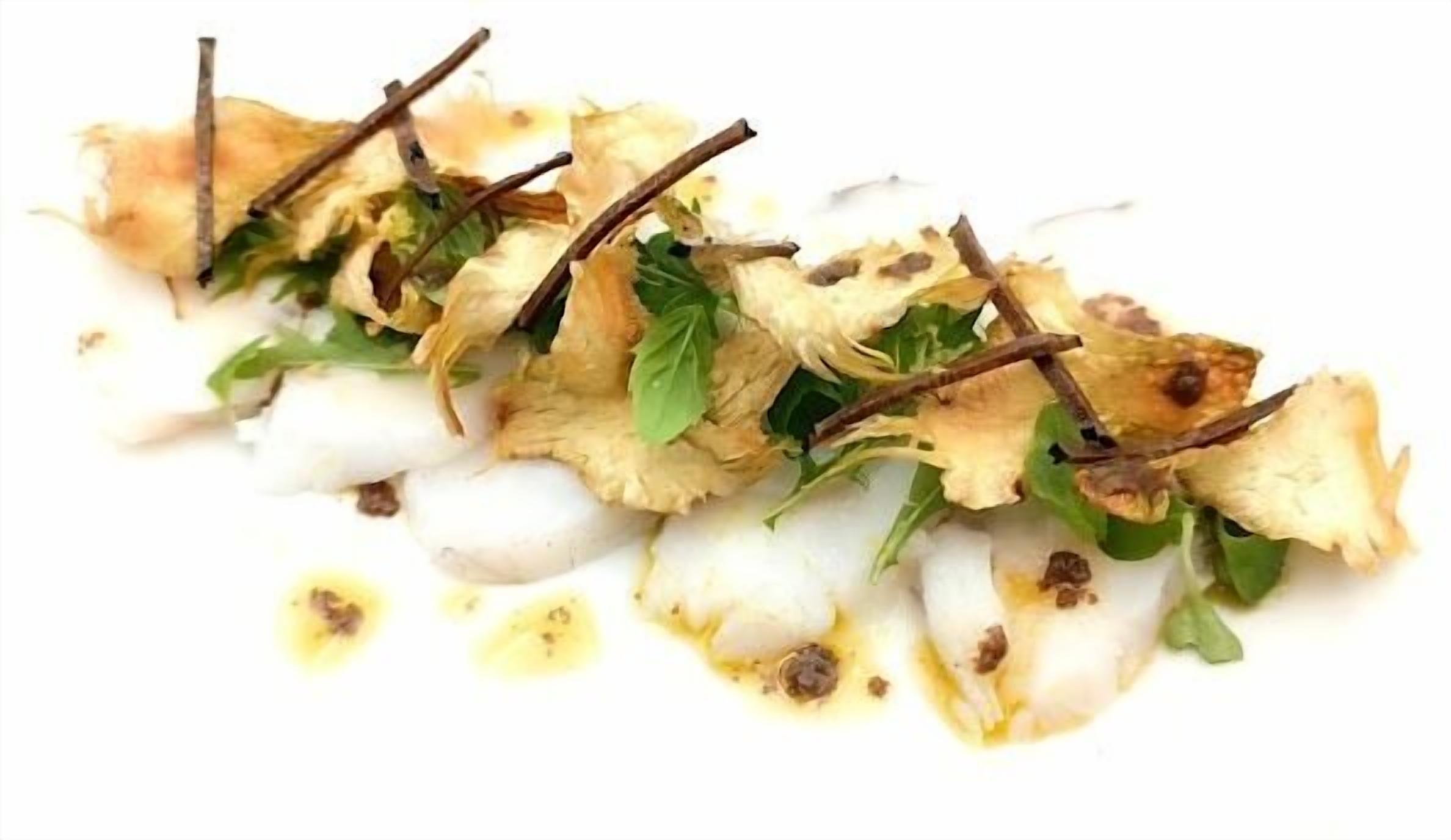 Un plato blanco con un guiso de esferas blancas, hojas verdes y ramitas marrones.