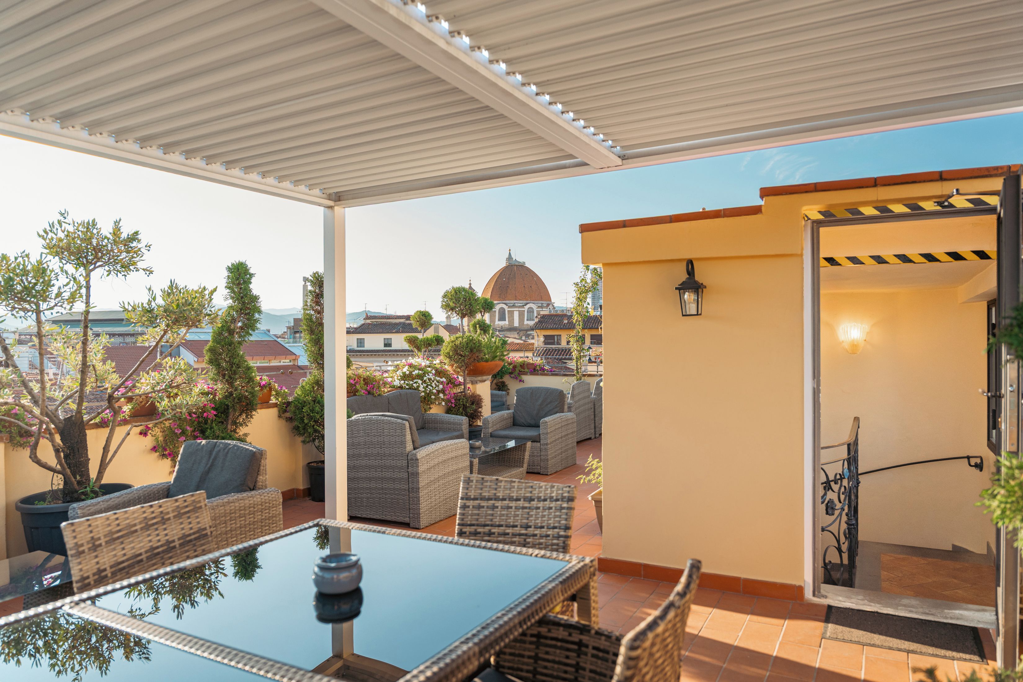 An outdoor patio with wicker furniture, a glass table, and a view of a dome-shaped building in the distance.