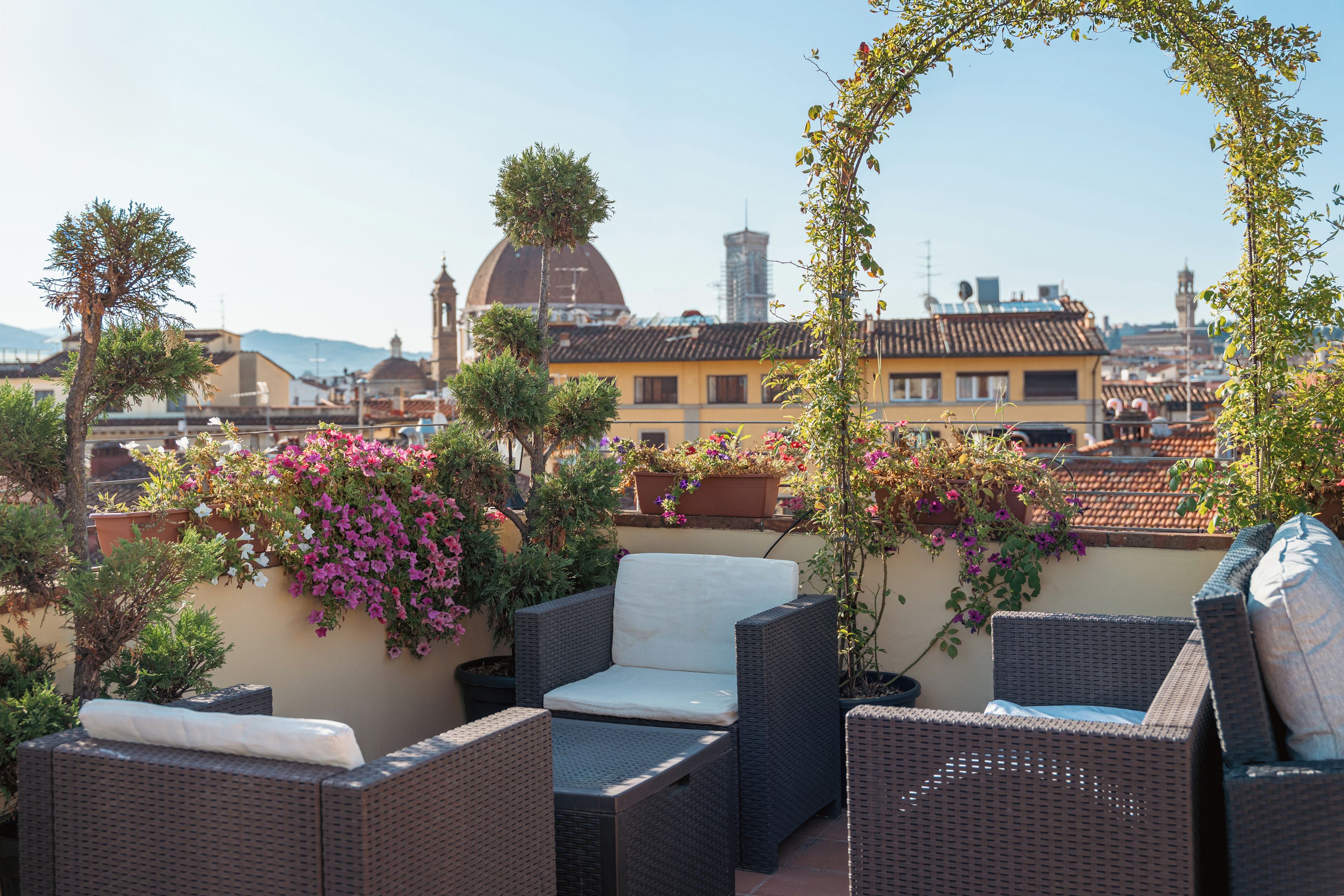 A rooftop terrace with wicker furniture, potted plants, and a view of the cityscape.