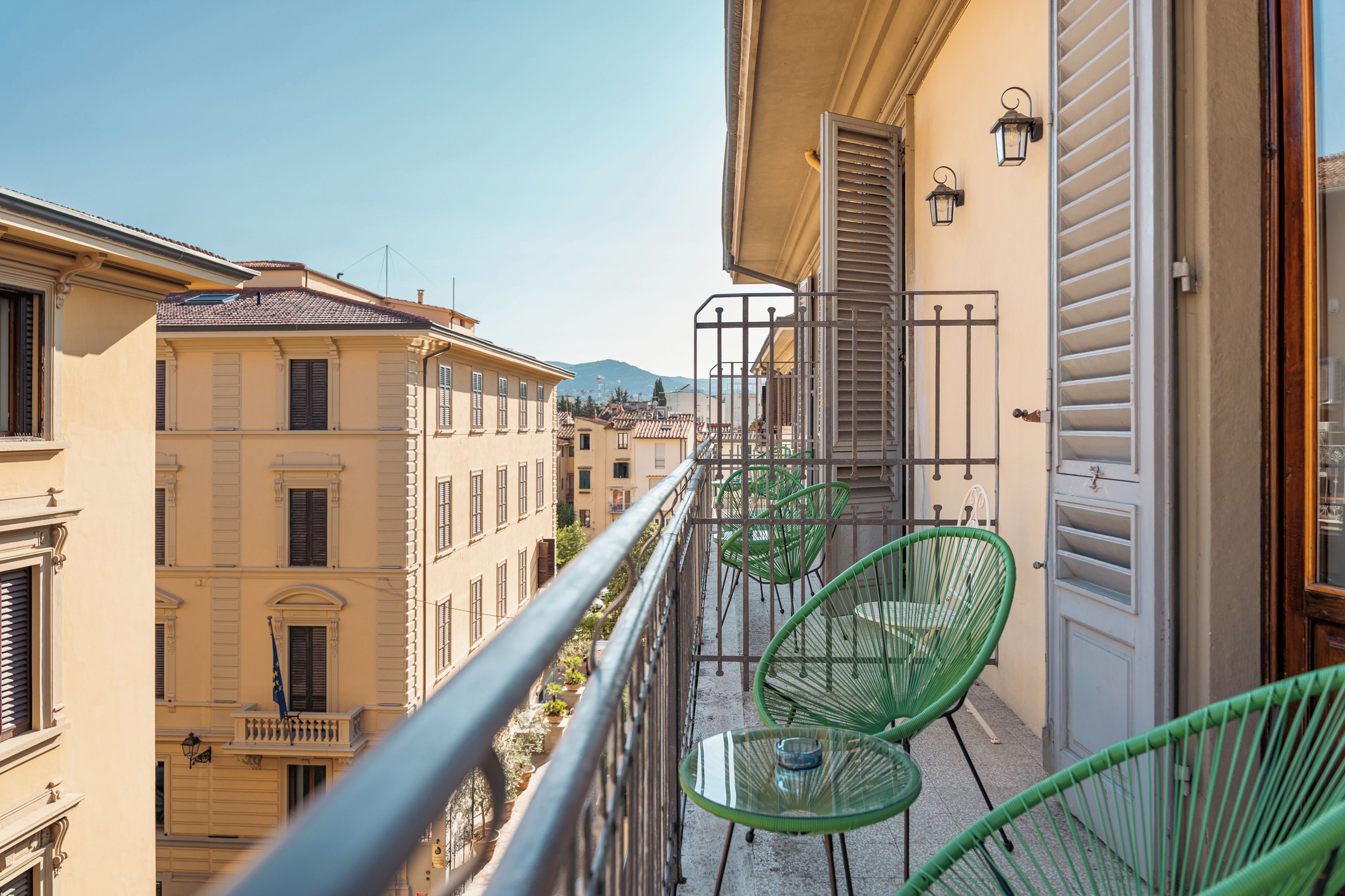 Un balcon avec une balustrade en métal, une table en verre et deux chaises vertes.