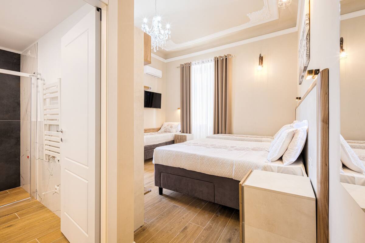 A modern hotel room with a large bed, a bedside table, a TV, and a chandelier.