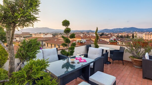 A terrace with wicker furniture, a glass table, and potted plants. - Hotel Bijou Roof Terrace (Florence)