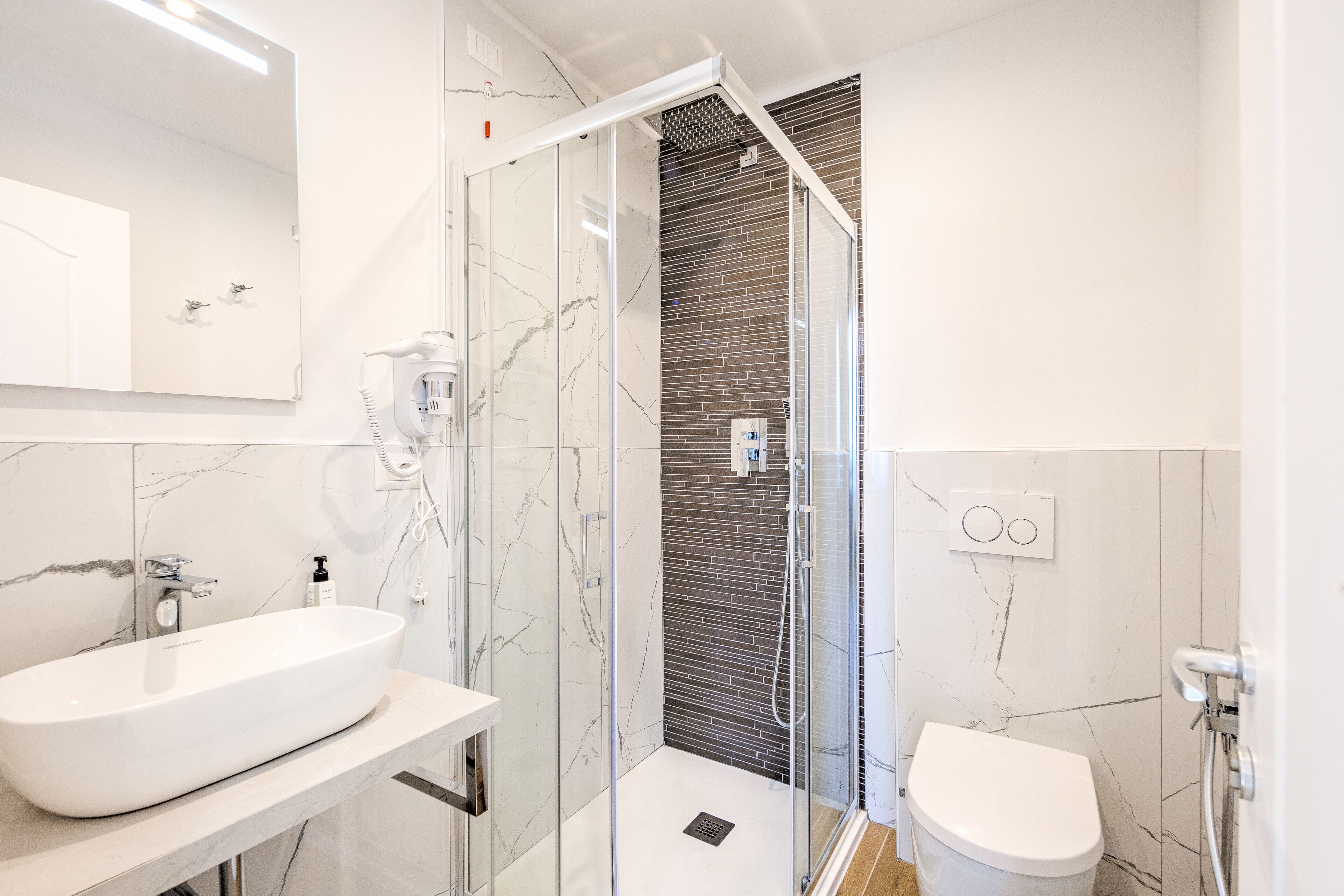 A modern bathroom with a large white sink, a glass-enclosed shower, and a toilet.