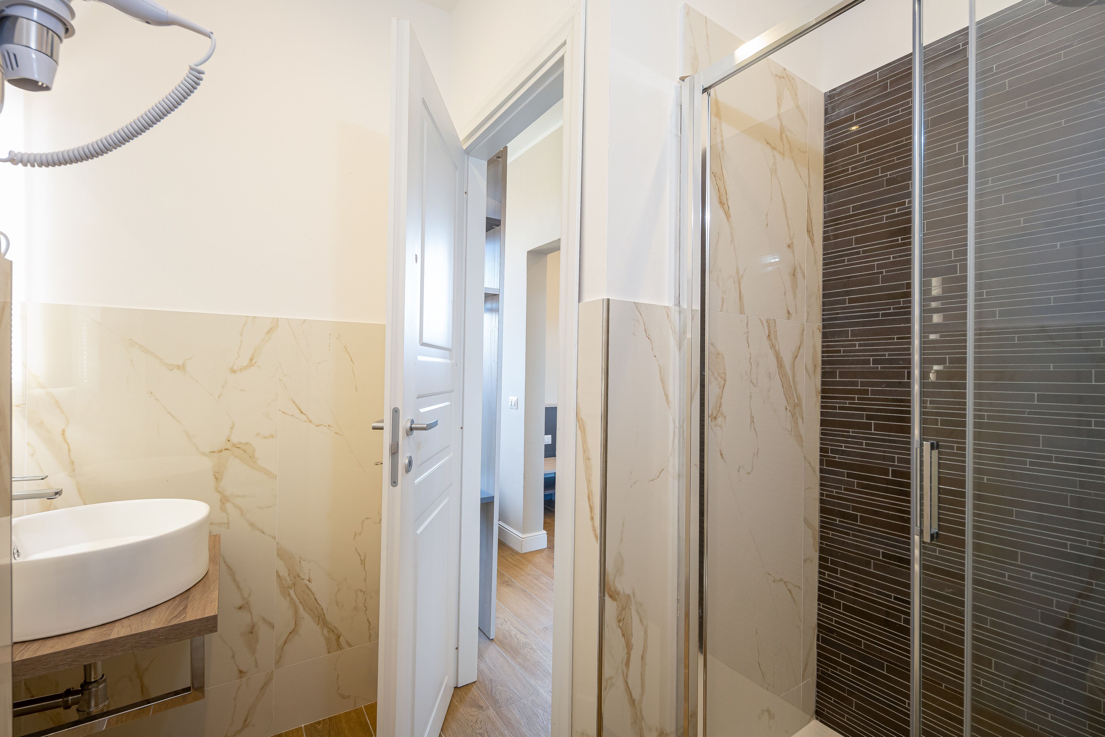 A bathroom with a sink, a shower, and a door leading to another room.