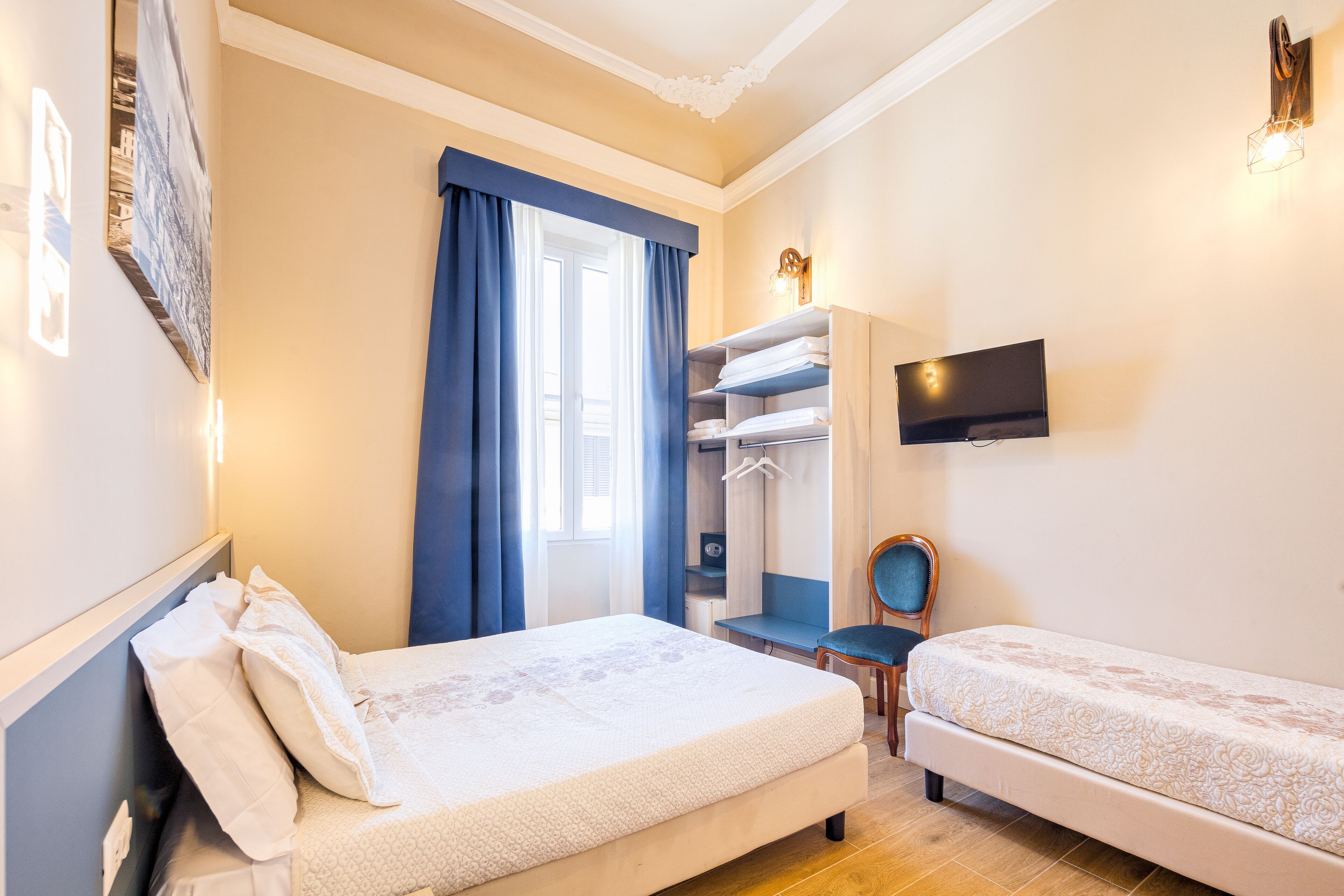 A hotel room with a bed, a desk, a chair, a TV, and a wardrobe.