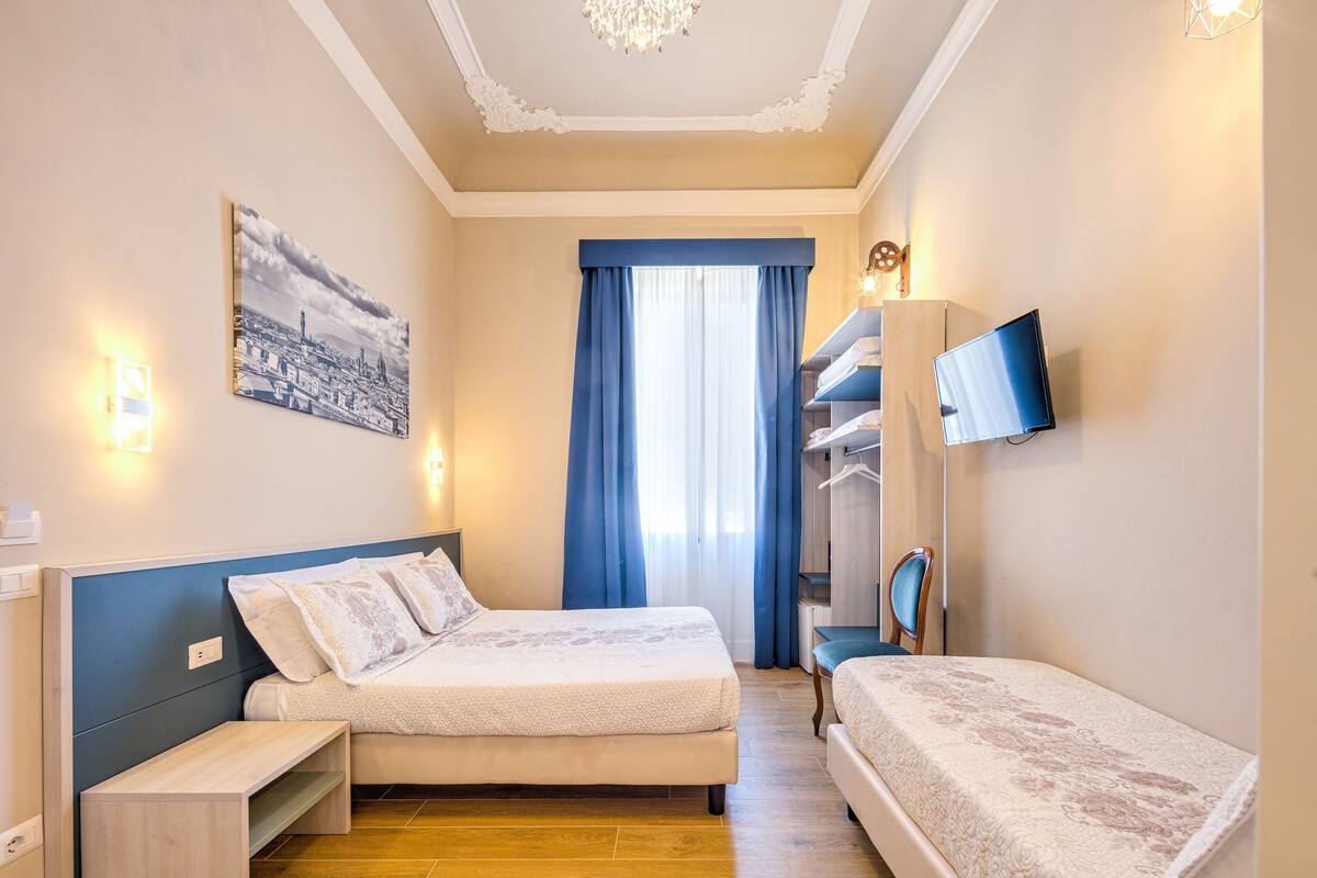 A hotel room with two beds, a TV, a wardrobe, and a window with curtains.