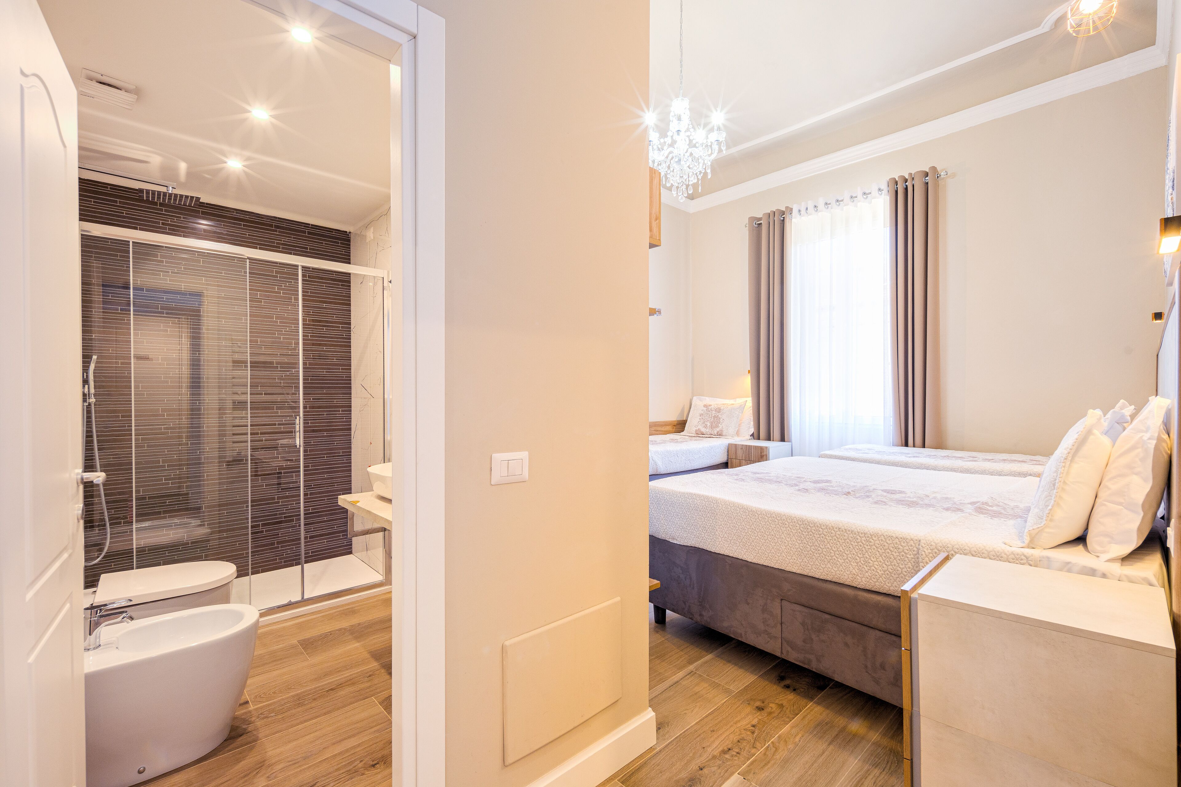 Une chambre à coucher moderne avec un grand lit, une salle de bain séparée dotée d’une douche à parois de verre et d’un lustre.
