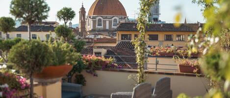 A terrace with outdoor furniture, potted plants, and a view of a historic building with a dome.