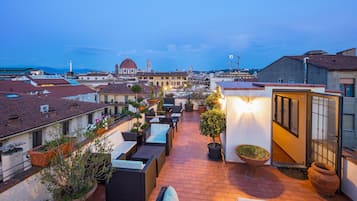 Una terraza en la azotea con mobiliario exterior, plantas en macetas y vistas de la ciudad.