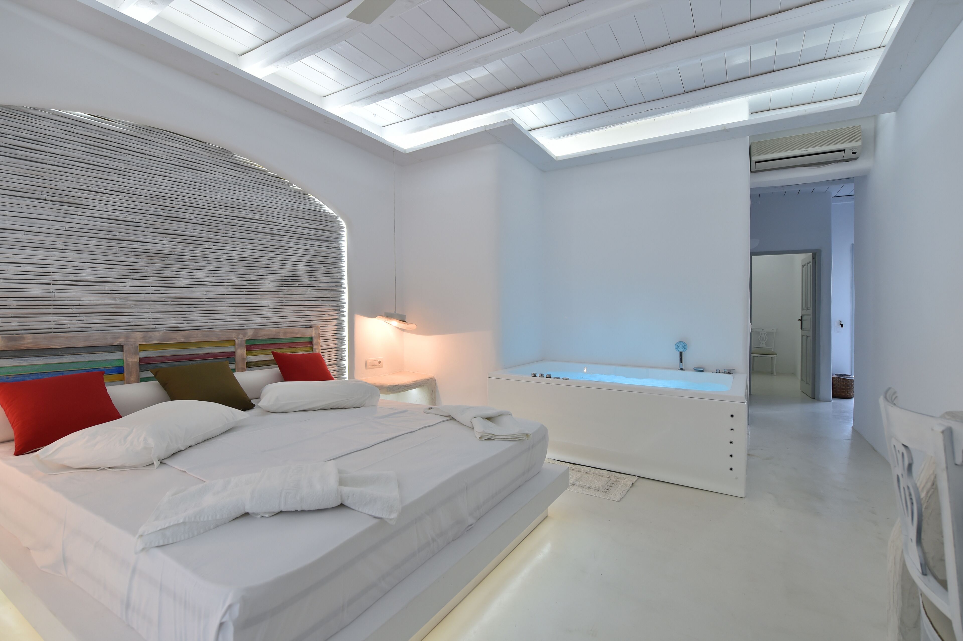 A modern bedroom with a skylight, a large bed, a white bathtub, and a walk-in closet.