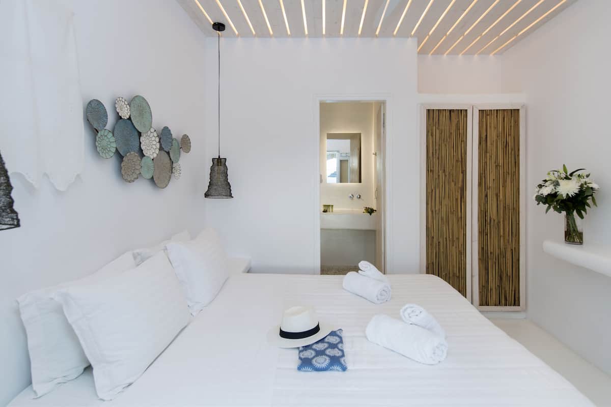 A modern hotel room with a neatly made bed, a hanging light fixture, a decorative wall piece, and a wooden door.