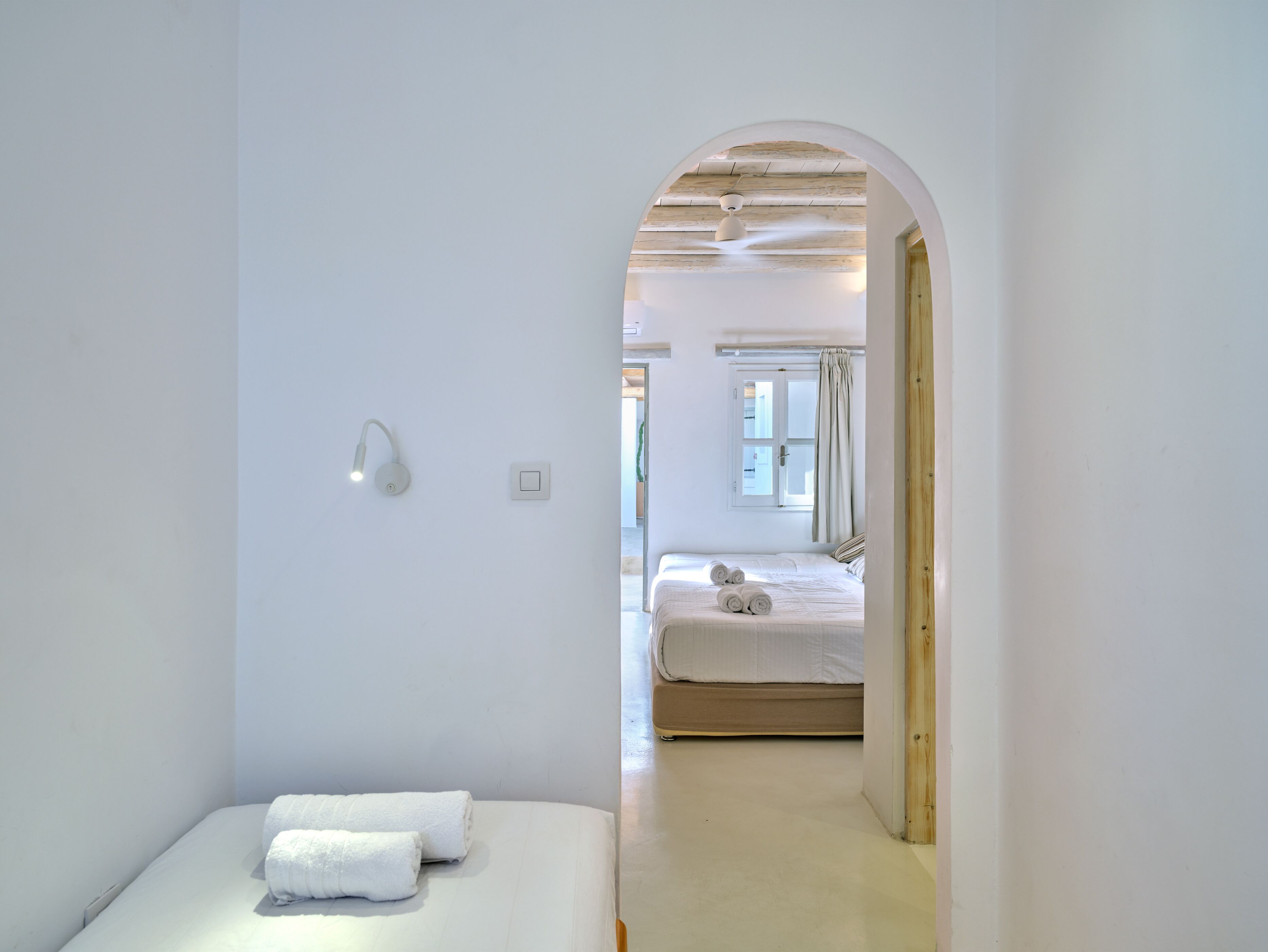 A minimalist bedroom with a single bed, a small bedside table, and a wall-mounted light fixture.