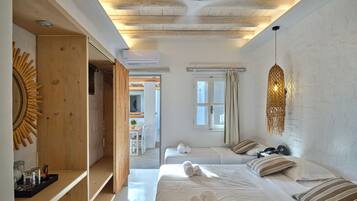 Ein modernes Schlafzimmer mit Holzboden, einem großen Bett mit aufgerollten Handtüchern, einer Hängeleuchte und Blick auf einen Essbereich.