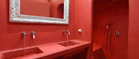 A bathroom with a red wall, a white ornate mirror, two sinks, and a shower area.