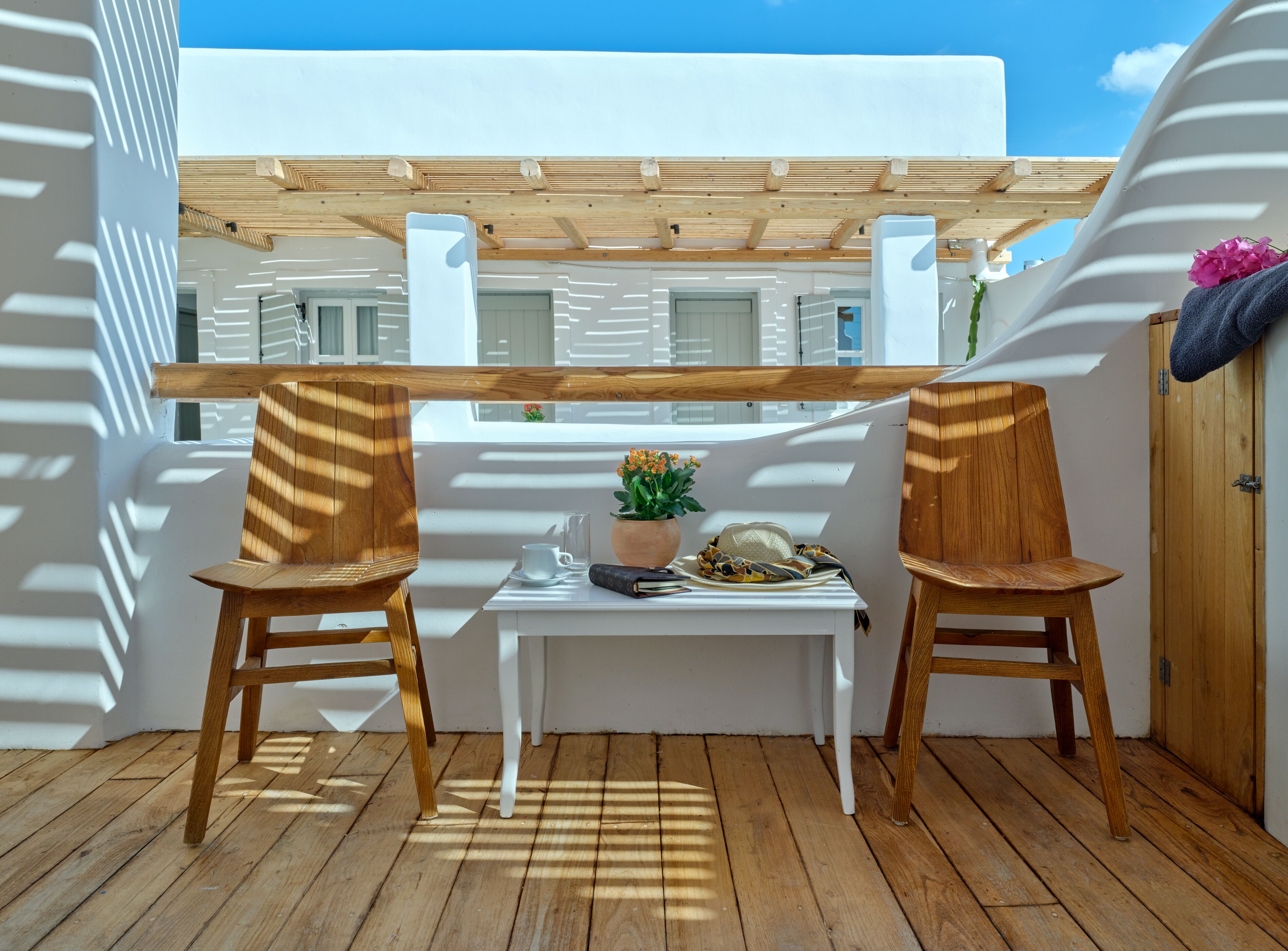 A wooden deck with two chairs and a small table, a potted plant, and a hat on the table.
