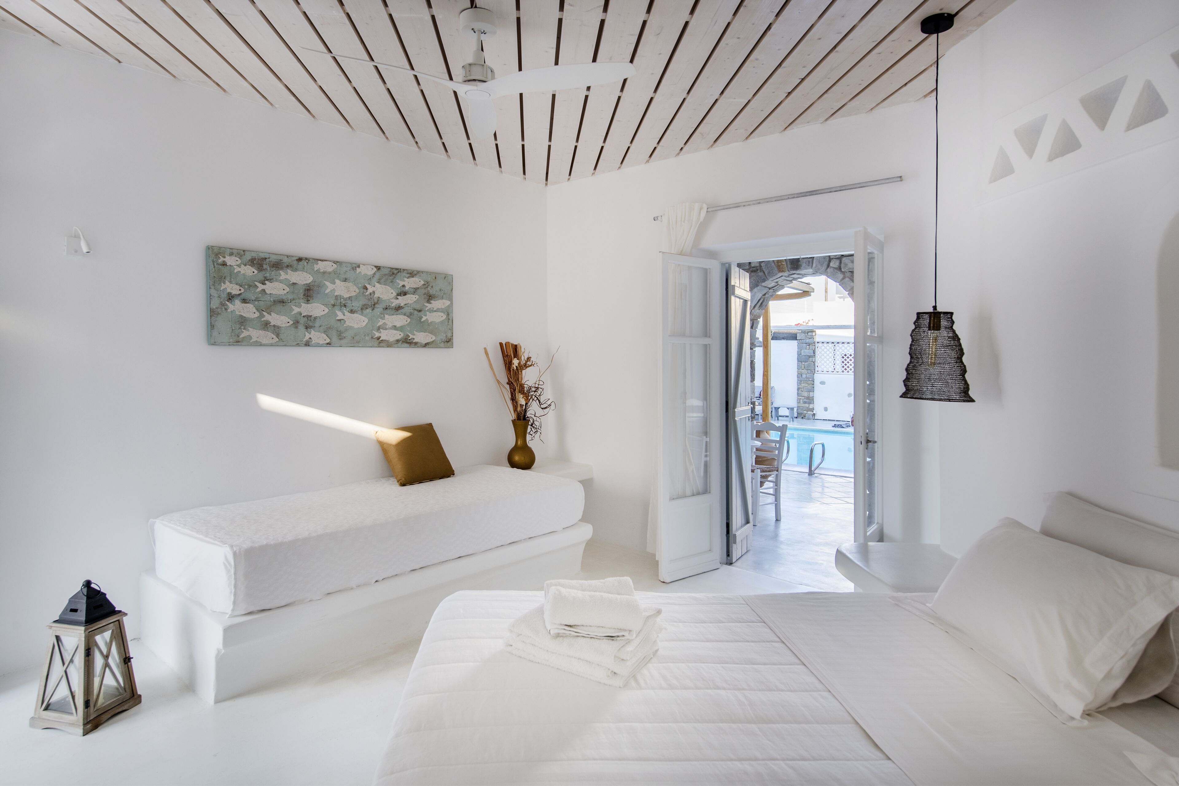 Une chambre moderne avec un lit blanc, un banc, un tableau et une vue sur un espace extérieur.