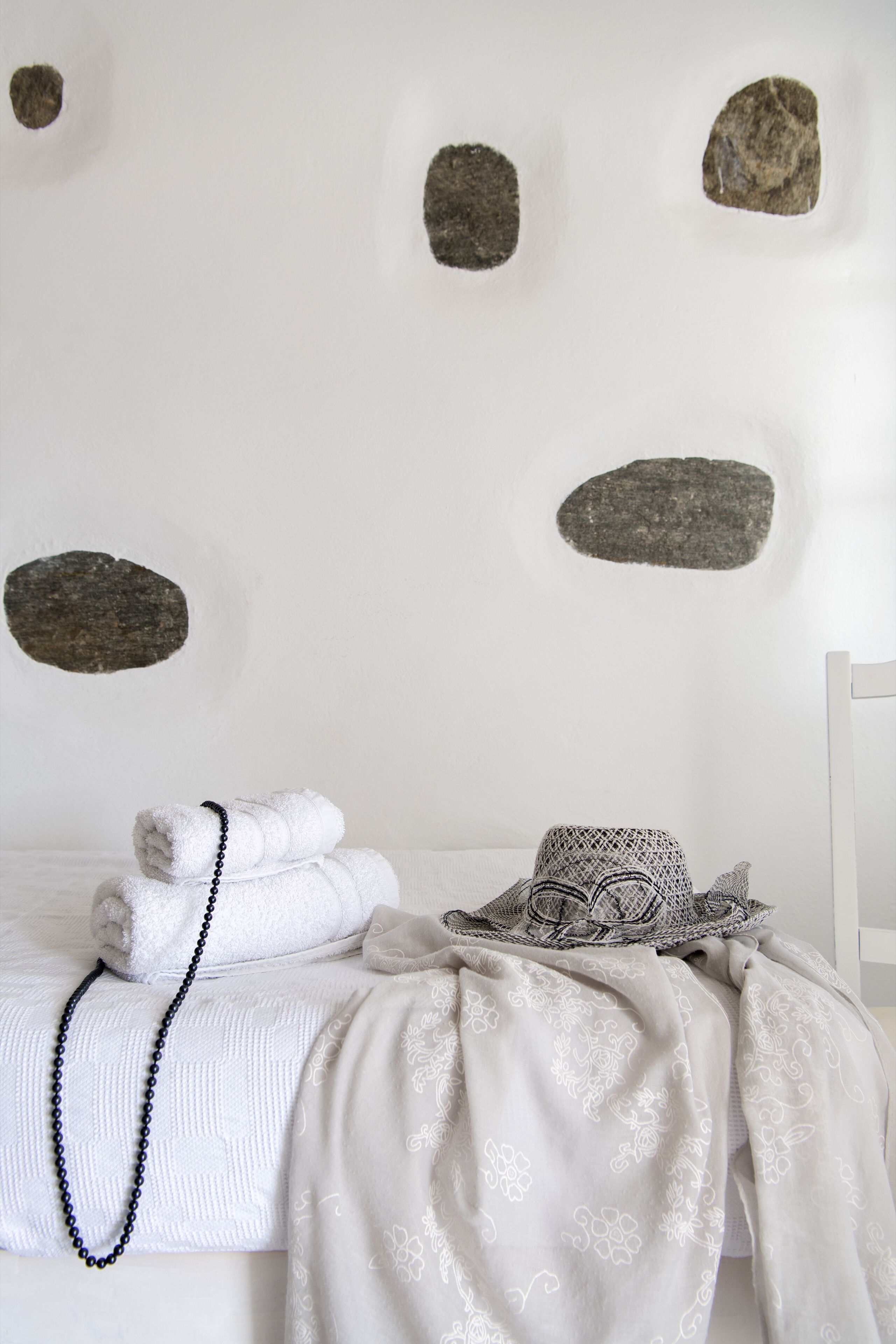 Una cama bien hecha con toallas y un collar de cuentas, un sombrero estampado y una pared decorativa con adornos que simulan piedra.