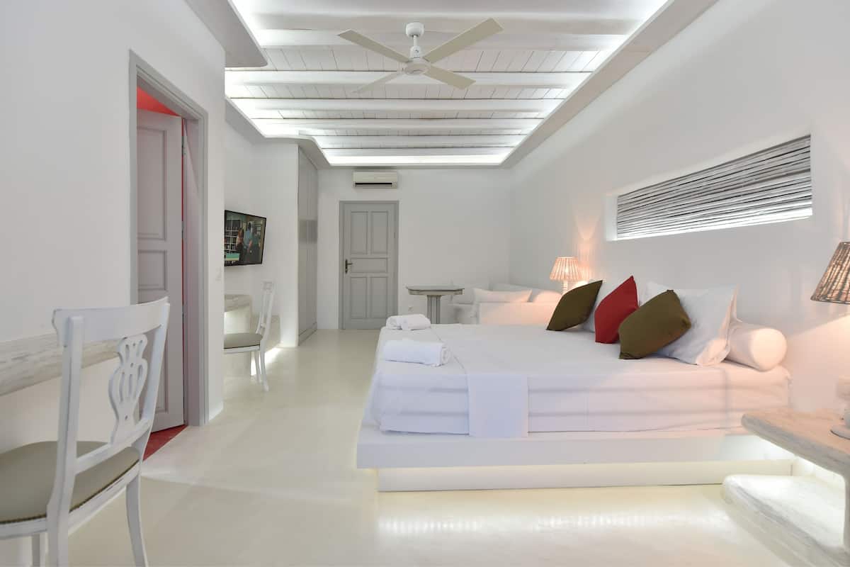 A modern hotel room with a large bed, a ceiling fan, a small table, and a TV mounted on the wall.