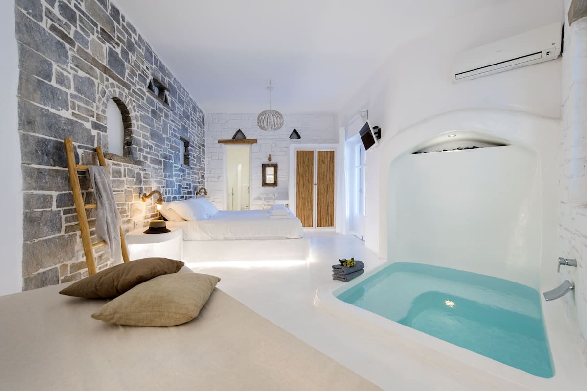 A modern spa room with a stone wall, a large bathtub, and a cozy seating area.