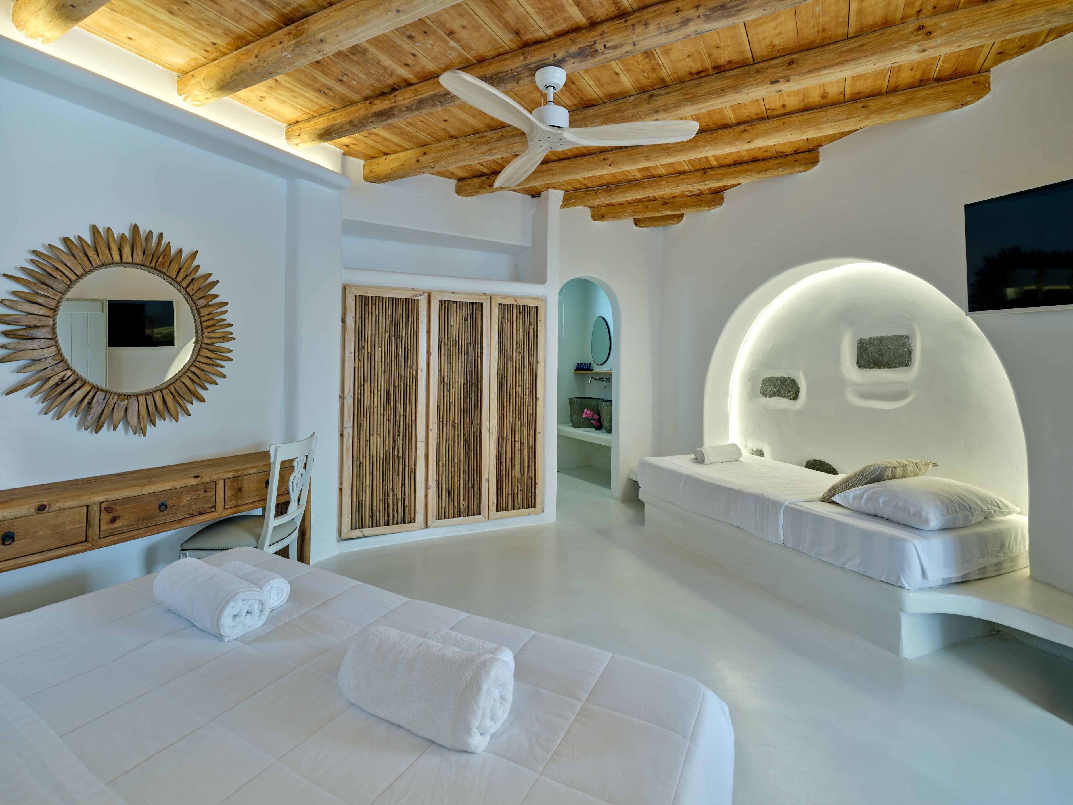 A modern bedroom with a wooden ceiling, a large mirror, a vanity, and a unique curved bed.