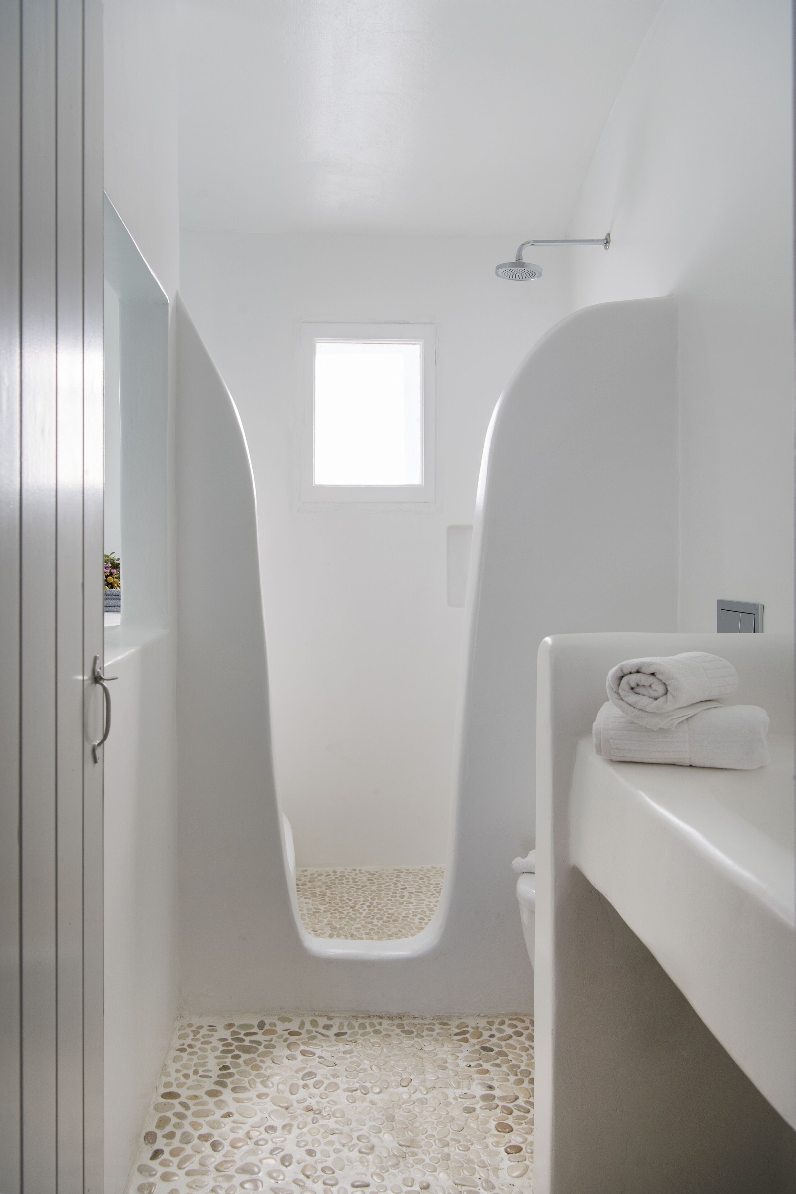 A bathroom with a shower, a small window, and a towel on a shelf.
