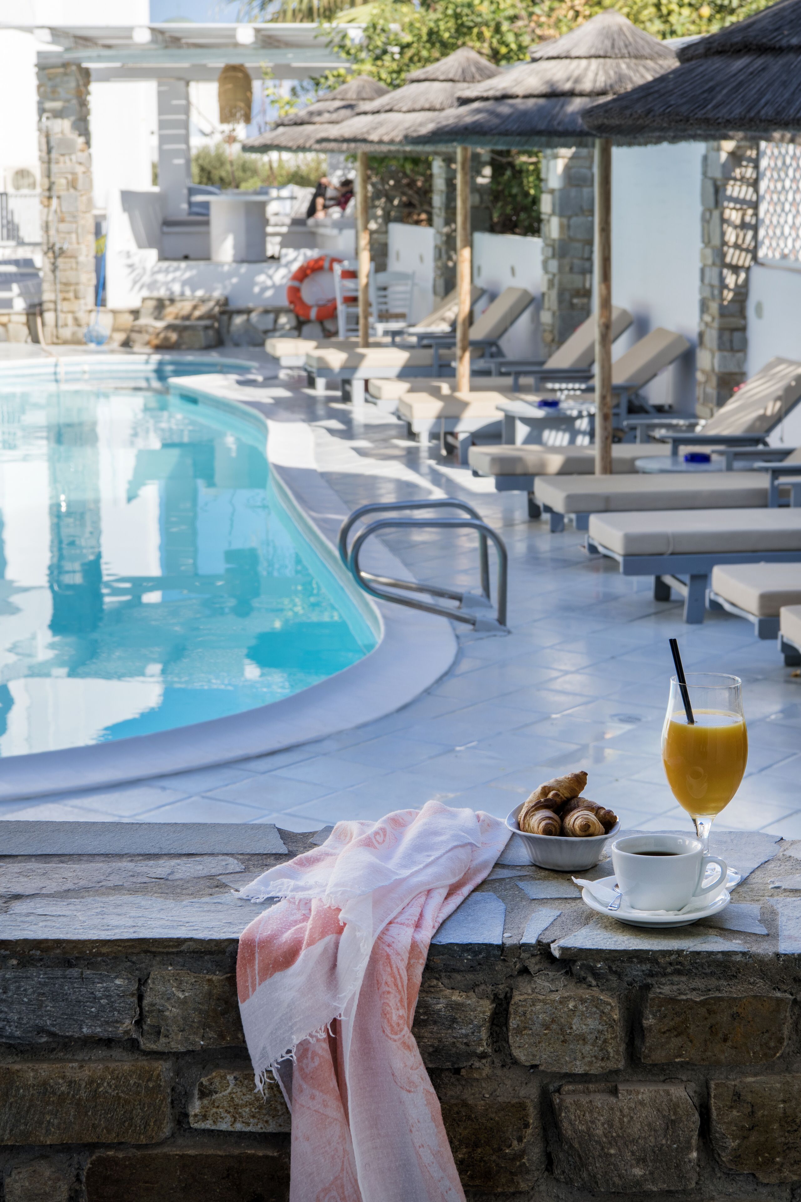 A poolside area with lounge chairs, a stone wall, and a table with a drink and pastries.