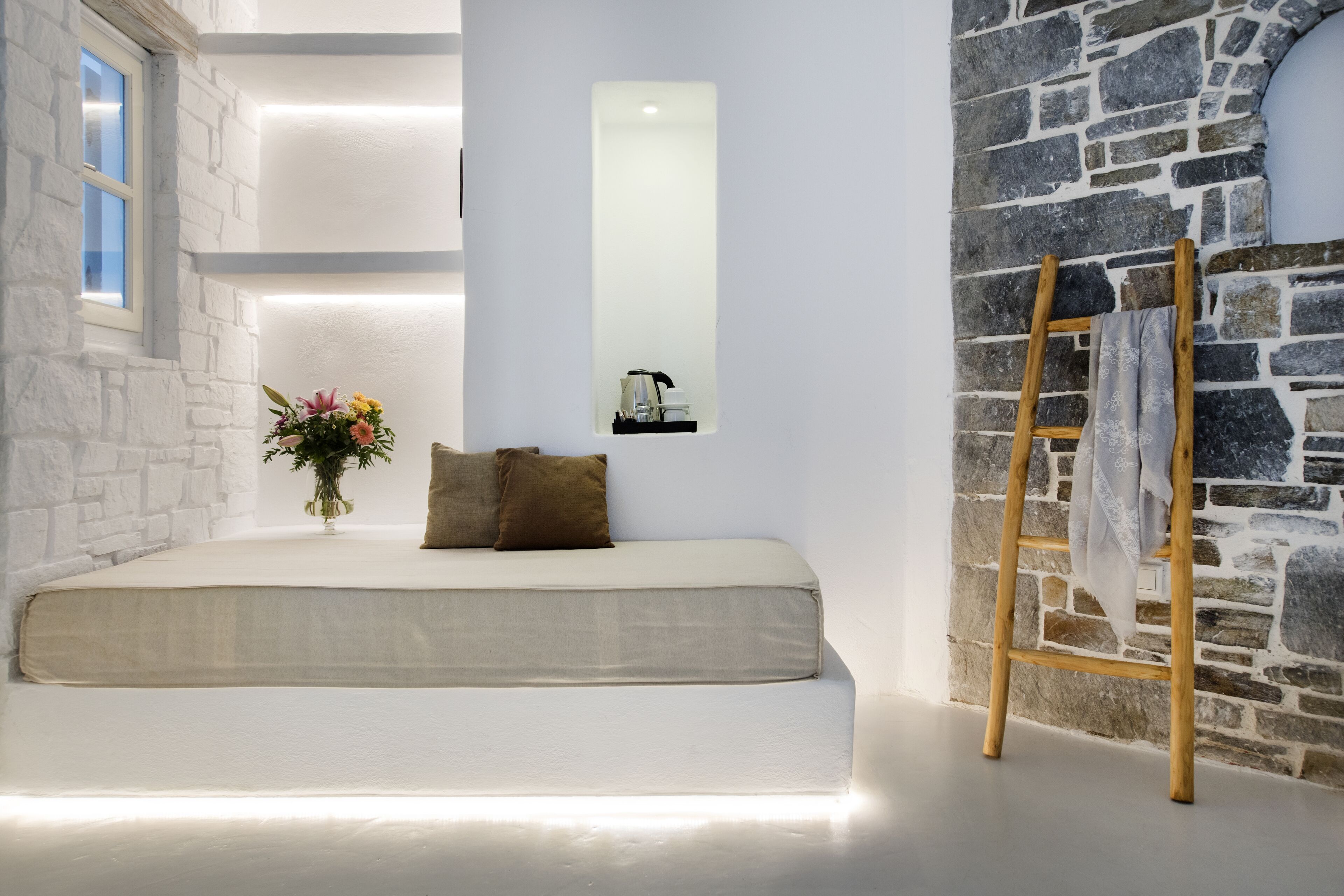A bedroom with a bed, a wooden ladder, a stone wall, and a window.