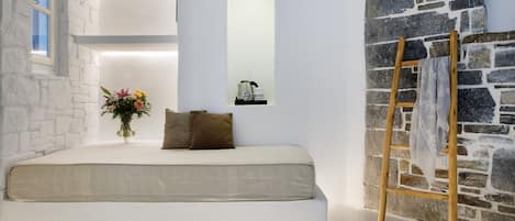 A bedroom with a bed, a wooden ladder, a stone wall, and a window.