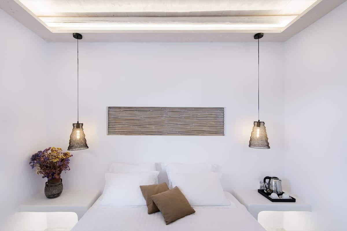 A modern bedroom with a bed, bedside tables, a vase with flowers, and pendant lights.