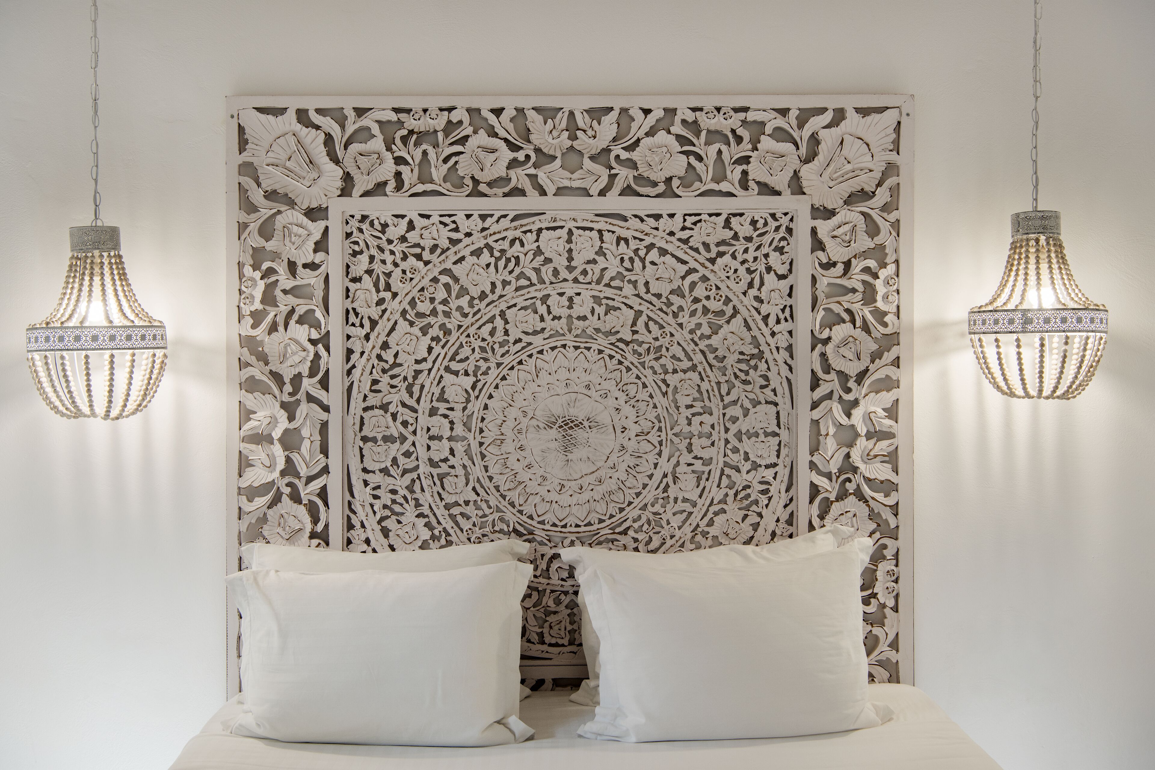 A bedroom with a decorative headboard, two hanging light fixtures, and a bed with white bedding.